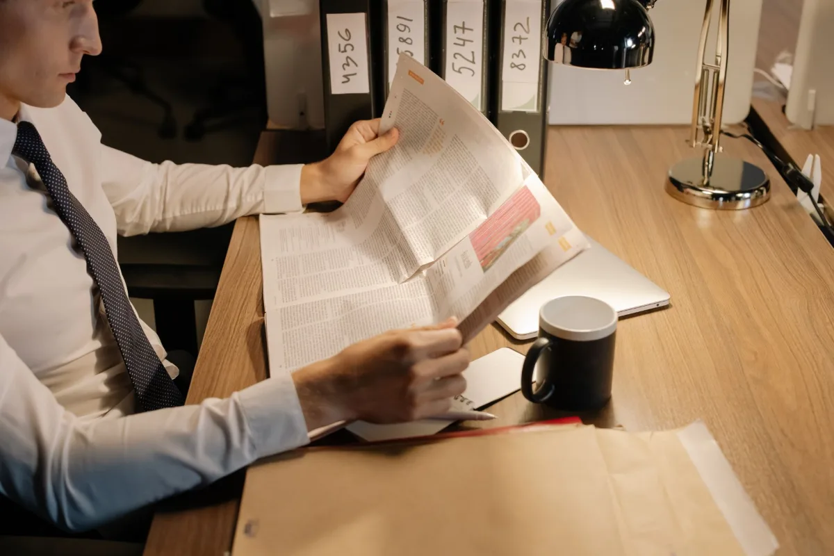 Um empresário concentrado lê um jornal em uma mesa de madeira em seu escritório, enfatizando trabalho e informação.